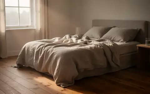 Ein minimalistisch eingerichtetes Schlafzimmer mit weichem Tageslicht, das durch ein Fenster auf ein ungemachtes Bett fällt. - Foto: über boerse-global.de