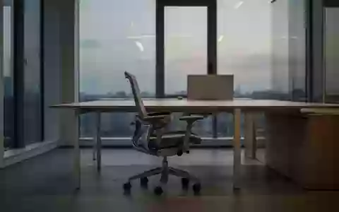 Ein leerer, minimalistischer Büroarbeitsplatz mit einem einzelnen Bürostuhl vor einem aufgeräumten Schreibtisch bei Dämmerung. - Foto: über boerse-global.de