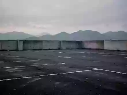 Leerer, asphaltierter Parkplatz mit verblassten Linien vor einer grauen Bergkulisse bei Dämmerung. - Foto: über boerse-global.de