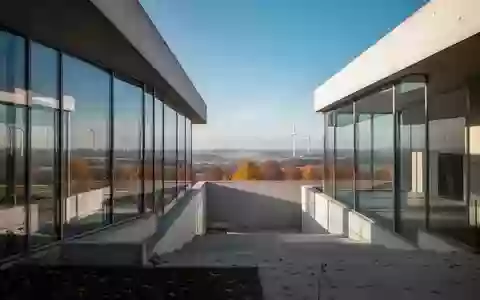 Moderne Industriearchitektur mit Glasfassaden und Windrädern in einer weiten deutschen Landschaft bei hellem Tageslicht. - Foto: über boerse-global.de
