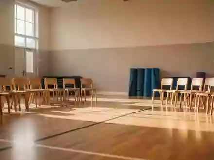 Ein heller, leerer Gymnastikraum in einem Bürgerhaus mit Holzboden und ordentlich aufgestellten Stühlen bei Tageslicht. - Foto: über boerse-global.de