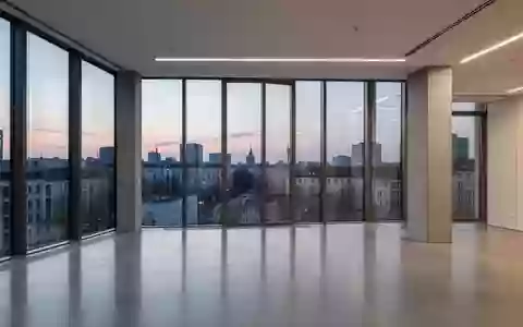 Modernes, minimalistisches Büro-Interieur mit großen Fenstern und Blick auf eine Berliner Skyline bei Dämmerung. - Foto: über boerse-global.de