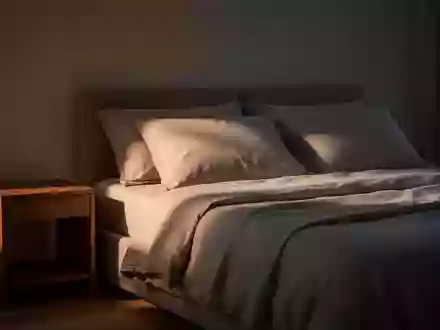 Ein minimalistisch eingerichtetes Schlafzimmer in der Abenddämmerung mit einem ungemachten Bett und einem Holznachttisch. - Foto: über boerse-global.de