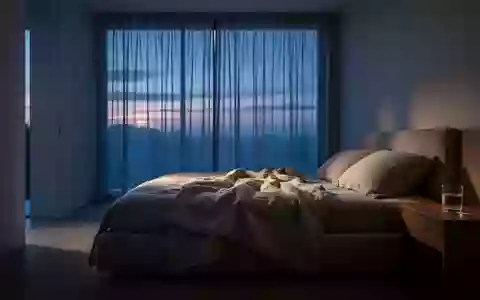 Ein minimalistisch eingerichtetes Schlafzimmer in der Morgendämmerung mit einem ungemachten Bett und weichem Lichteinfall. - Foto: über boerse-global.de