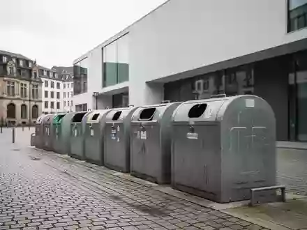 Leere öffentliche Müllbehälter vor einer städtischen Kulisse in Freiburg als Symbol für die Debatte zur Verpackungssteuer. - Foto: über boerse-global.de