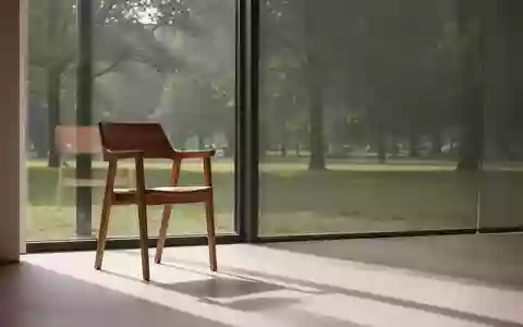 Ein leerer Holzstuhl an einem hellen Fenster mit Blick in einen ruhigen, grünen Park bei sanftem Tageslicht. - Foto: über boerse-global.de