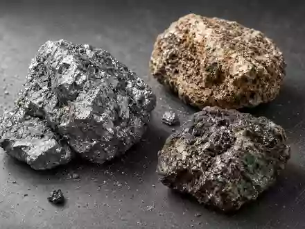 Nahaufnahme von rauen, industriellen Seltene-Erden-Mineralproben auf einer dunklen Werkbank bei natürlichem Licht. - Foto: über boerse-global.de