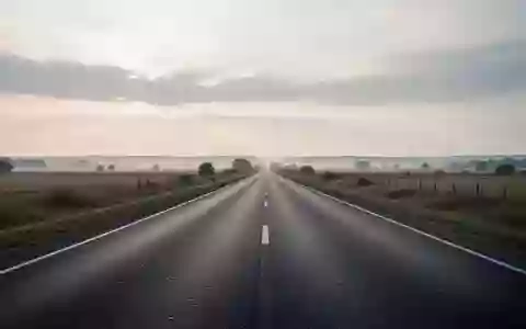 Eine leere, unbefahrene Landstraße erstreckt sich in einer weiten Landschaft unter einem bewölkten Himmel. - Foto: über boerse-global.de