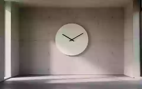 Eine minimalistische Wanduhr an einer schlichten Betonwand in einem hellen, leeren Raum. - Foto: über boerse-global.de