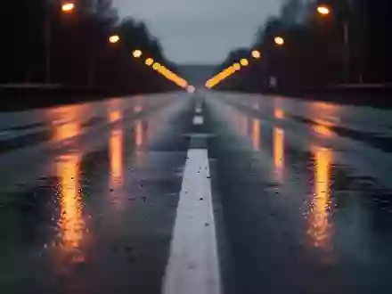 Eine menschenleere, nasse Asphaltstraße bei Dämmerung mit reflektierenden Fahrbahnmarkierungen und verschwommenen Straßenlaternen. - Foto: über boerse-global.de