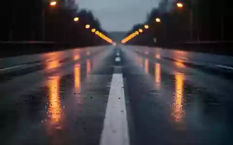Eine menschenleere, nasse Asphaltstraße bei Dämmerung mit reflektierenden Fahrbahnmarkierungen und verschwommenen Straßenlaternen. - Foto: über boerse-global.de