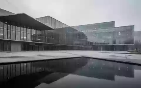 Modernes Verwaltungsgebäude aus Glas und Stahl spiegelt sich in einer Wasserfläche vor einem bewölkten Himmel. - Foto: über boerse-global.de