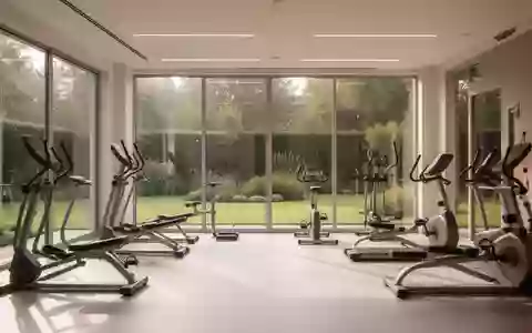 Ein heller, minimalistischer Rehabilitationsraum mit Fitnessgeräten und großen Fenstern mit Blick ins Grüne. - Foto: über boerse-global.de