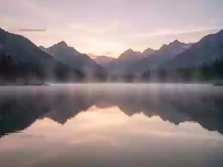 Ein ruhiger Bergsee bei Sonnenaufgang mit spiegelglatter Wasseroberfläche und leichtem Morgennebel. - Foto: über boerse-global.de