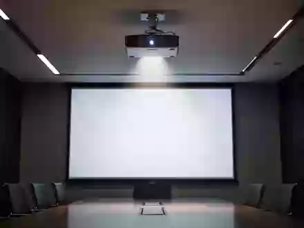 Ein moderner, abgedunkelter Konferenzraum mit einem Deckenprojektor, der auf eine leere, weiĂźe Leinwand strahlt. - Foto: ĂĽber boerse-global.de
