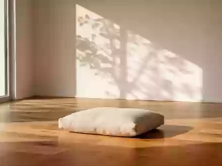 Ein minimalistischer, heller Meditationsraum mit einem einzelnen beigen Sitzkissen auf einem Holzboden und sanftem Tageslicht. - Foto: über boerse-global.de