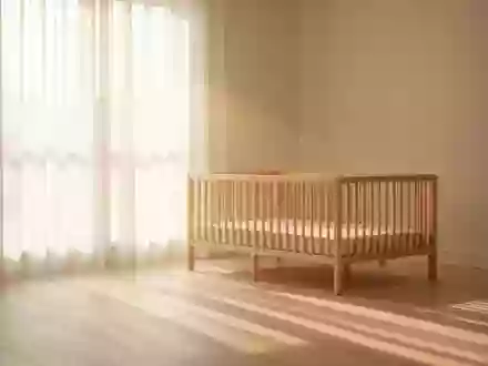 Ein sonnendurchflutetes, minimalistisch eingerichtetes Kinderzimmer mit einem leeren Holzbettchen im weichen Morgenlicht. - Foto: über boerse-global.de
