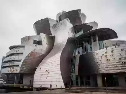 Die geschwungene, metallisch glänzende Fassade der Düsseldorfer Gehry-Bauten vor einem bewölkten Himmel. - Foto: über boerse-global.de