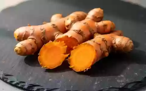 Frische Kurkuma-Wurzeln mit leuchtend orangem Inneren auf einer dunklen Schieferplatte. - Foto: über boerse-global.de