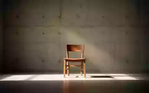 Ein minimalistischer Raum mit einem einzelnen Holzstuhl in einem sanften Lichtkegel vor einer schlichten Betonwand. - Foto: über boerse-global.de