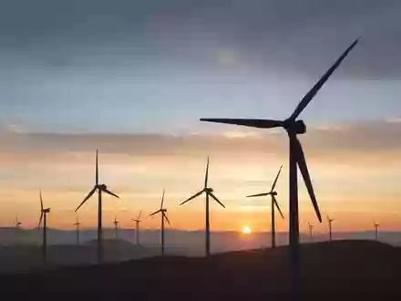Moderne Windkraftanlagen bei Sonnenaufgang auf einem weitläufigen Feld. - Foto: über boerse-global.de