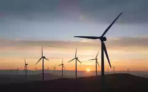 Moderne Windkraftanlagen bei Sonnenaufgang auf einem weitläufigen Feld. - Foto: über boerse-global.de