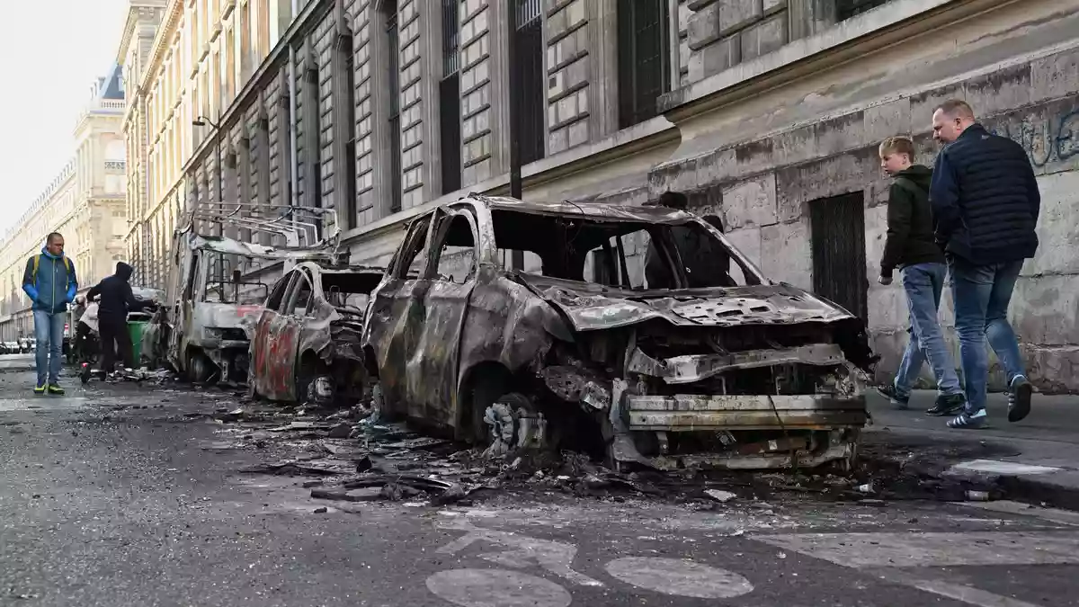 Passanten beäugen ausgebrannte Autos in Paris. - Bild: Emma Da Silva/AP/dpa
