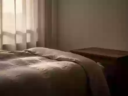 Ein minimalistisch eingerichtetes Schlafzimmer mit weichem Morgenlicht, das auf ein ungemachtes Bett aus Leinen fällt. - Foto: über boerse-global.de