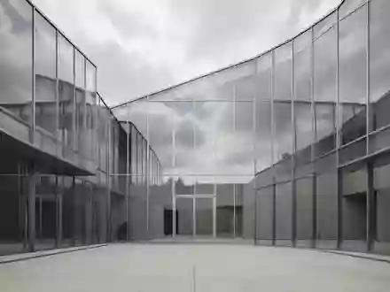 Ein modernes, minimalistisches Gebäude aus Glas und Stahl spiegelt den bewölkten Himmel in einem leeren Innenhof wider. - Foto: über boerse-global.de