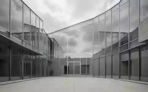 Ein modernes, minimalistisches Gebäude aus Glas und Stahl spiegelt den bewölkten Himmel in einem leeren Innenhof wider. - Foto: über boerse-global.de