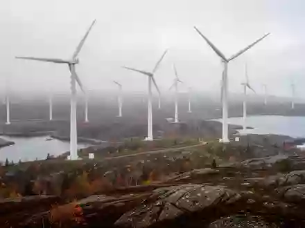 Weite Küstenlandschaft in Nova Scotia mit großen Windkraftanlagen auf einer felsigen Anhöhe bei nebligem Morgenlicht. - Foto: über boerse-global.de