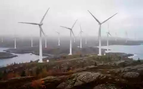 Weite Küstenlandschaft in Nova Scotia mit großen Windkraftanlagen auf einer felsigen Anhöhe bei nebligem Morgenlicht. - Foto: über boerse-global.de