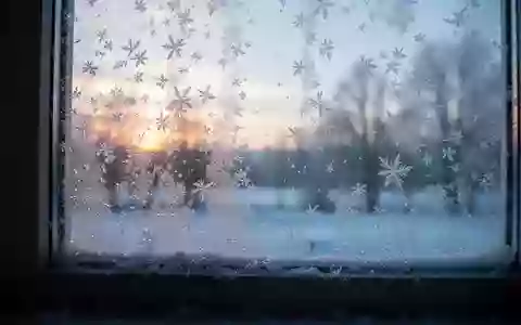 Mit Raureif bedeckte Fensterscheibe bei Sonnenaufgang mit Blick auf eine winterliche Landschaft. - Foto: über boerse-global.de