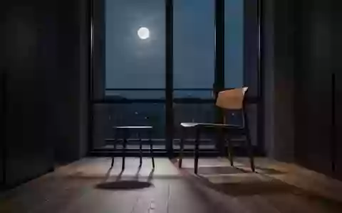 Ein minimalistisch eingerichteter, dunkler Raum mit einem leeren Stuhl bei Dämmerung und sanftem Mondlicht. - Foto: über boerse-global.de