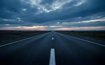 Eine leere, asphaltierte Straße bei Dämmerung unter einem bewölkten Himmel. - Foto: über boerse-global.de