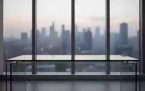 Ein minimalistischer, leerer Arbeitsplatz an einem Fenster mit Blick auf eine verschwommene Stadt bei Dämmerung. - Foto: über boerse-global.de