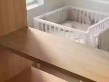 Ein minimalistisches, leeres Holzregal in einem hellen Kinderzimmer mit Blick auf ein schlichtes Babybett. - Foto: über boerse-global.de