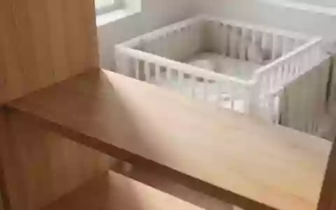 Ein minimalistisches, leeres Holzregal in einem hellen Kinderzimmer mit Blick auf ein schlichtes Babybett. - Foto: über boerse-global.de