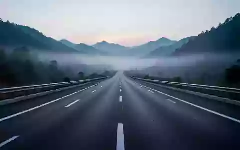 Eine weitläufige, leere Autobahn in einer nebligen Berglandschaft bei Dämmerung, die den Fokus auf die Infrastruktur legt. - Foto: über boerse-global.de