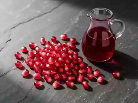 Frische Granatapfelkerne und ein Glas Granatapfelsaft auf einem dunklen Steintisch. - Foto: über boerse-global.de