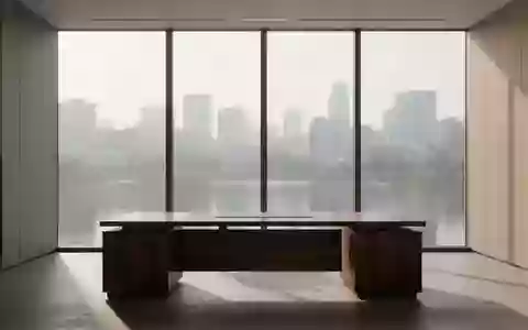 Ein minimalistisch eingerichtetes, leeres Büro mit einem dunklen Holztisch vor einer großen Fensterfront. - Foto: über boerse-global.de