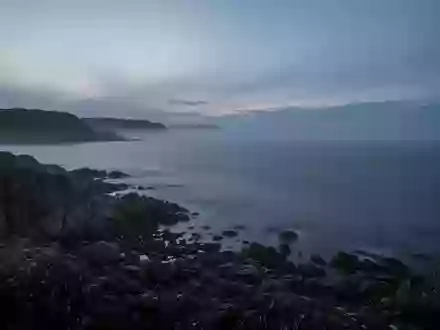Eine ruhige, neblige Küstenlandschaft am Abend mit Blick auf das offene Meer und felsige Uferabschnitte. - Foto: über boerse-global.de