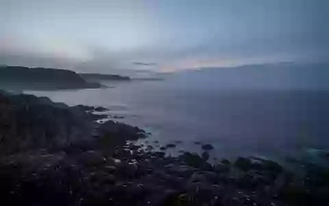 Eine ruhige, neblige Küstenlandschaft am Abend mit Blick auf das offene Meer und felsige Uferabschnitte. - Foto: über boerse-global.de