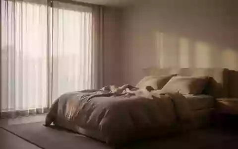 Ein minimalistisch eingerichtetes Schlafzimmer mit sanftem Tageslicht, das durch Vorhänge fällt und eine ruhige Atmosphäre schafft. - Foto: über boerse-global.de