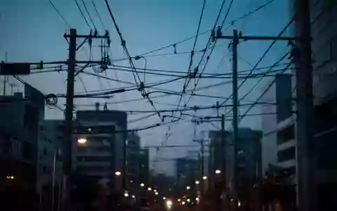 Stromleitungen und Telekommunikationskabel vor einem tiefblauen Abendhimmel über einer Stadt. - Foto: über boerse-global.de