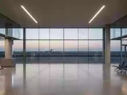 Ein moderner, leerer Flughafen-Abflugbereich mit großen Glasfronten und Blick auf das Rollfeld bei Dämmerung. - Foto: über boerse-global.de