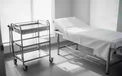 Ein heller, minimalistischer Behandlungsraum in einer modernen Klinik mit einem leeren Patientenbett und einem Metallwagen. - Foto: über boerse-global.de