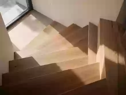 Eine minimalistische, sonnendurchflutete Holztreppe in einem modernen Haus, die den Fokus auf Struktur und Architektur legt. - Foto: über boerse-global.de