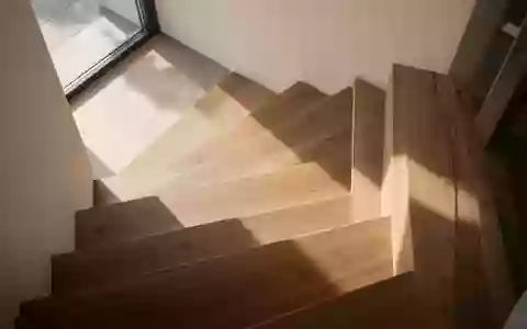 Eine minimalistische, sonnendurchflutete Holztreppe in einem modernen Haus, die den Fokus auf Struktur und Architektur legt. - Foto: über boerse-global.de