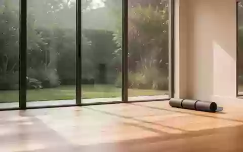 Ein minimalistischer, lichtdurchfluteter Übungsraum mit Holzboden und einer zusammengerollten Yogamatte vor einem Gartenblick. - Foto: über boerse-global.de
